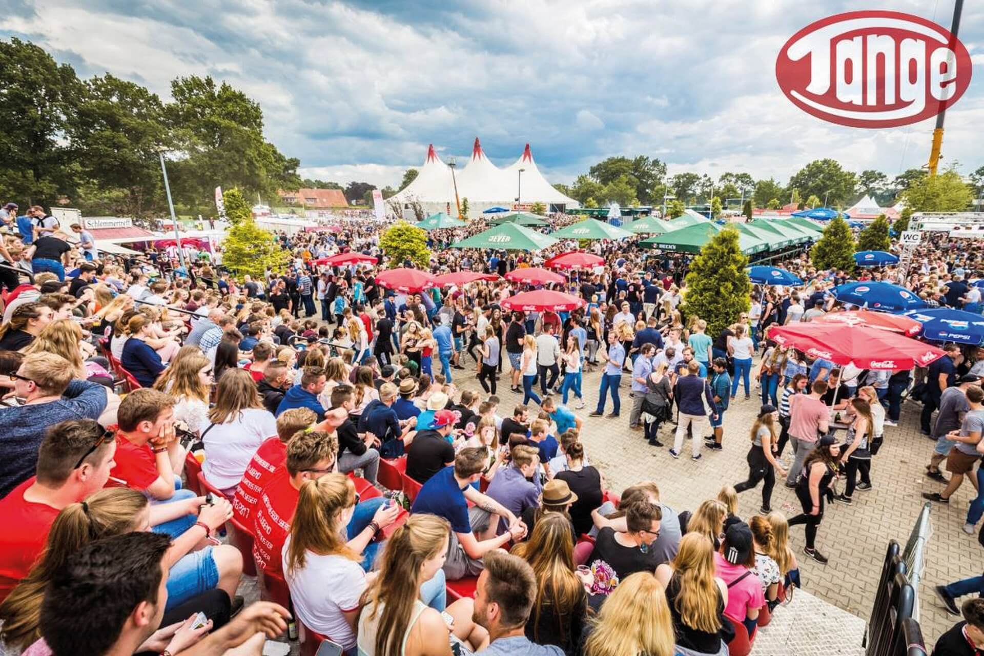 Das Bild zeigt viele Menschen auf einem Festgelände mit Sonnenschirmen und Pavillions